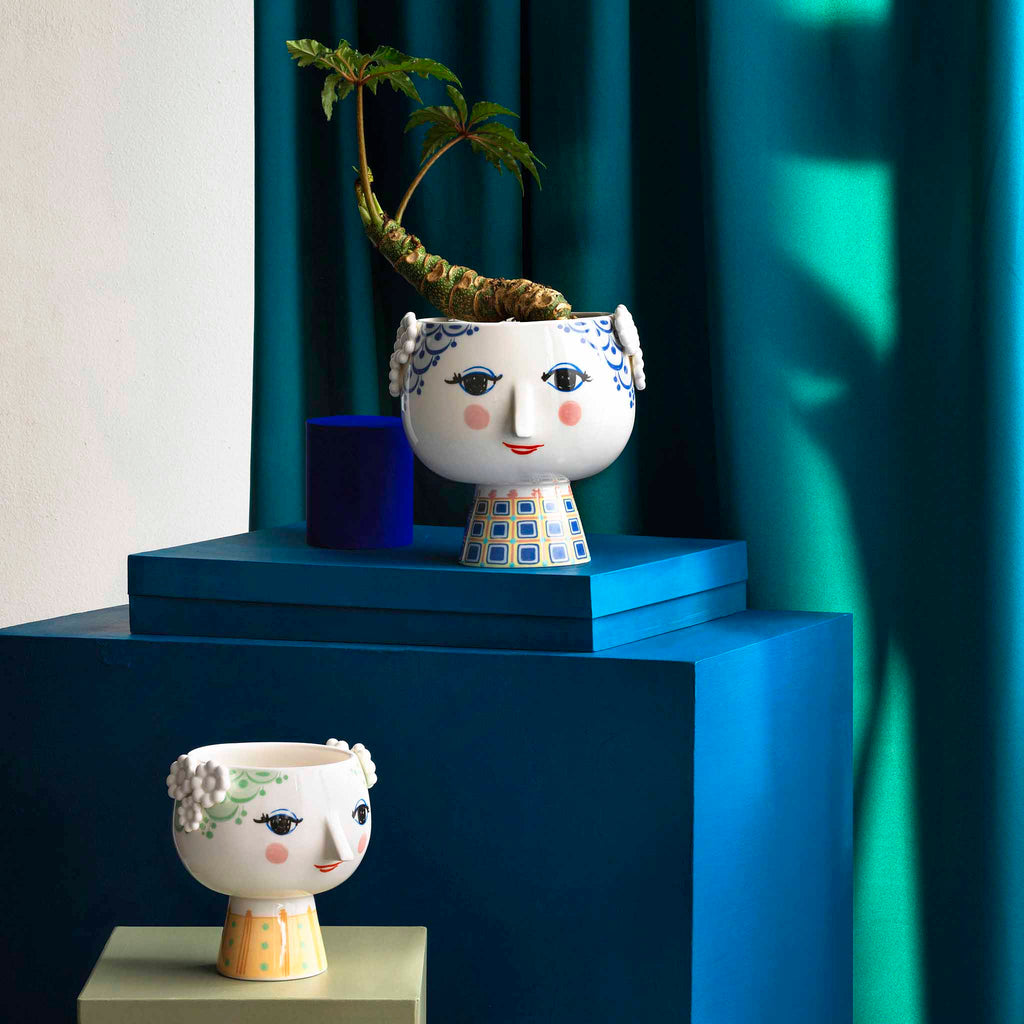 Eva flowerpot is made of glossy glazed ceramic with colorful decal and is inspired by Wiinblad's original EVA vases, which had wide heads with floral decorations and a cone-shaped body. The delicate face is from Wiinblad's original line, and the dress pattern is an interpretation of Bjørn Wiinblad's illustrations.
