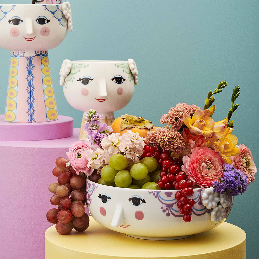 The range is made from glossy-glazed porcelain with colourful patterns and floral reliefs. With her cheerful smile, blushing cheeks, and colourful decorations, Eva embodies the essence of Bjørn Wiinblad as a person and artist – whether in the shape of a vase, candlestick or flower pot.