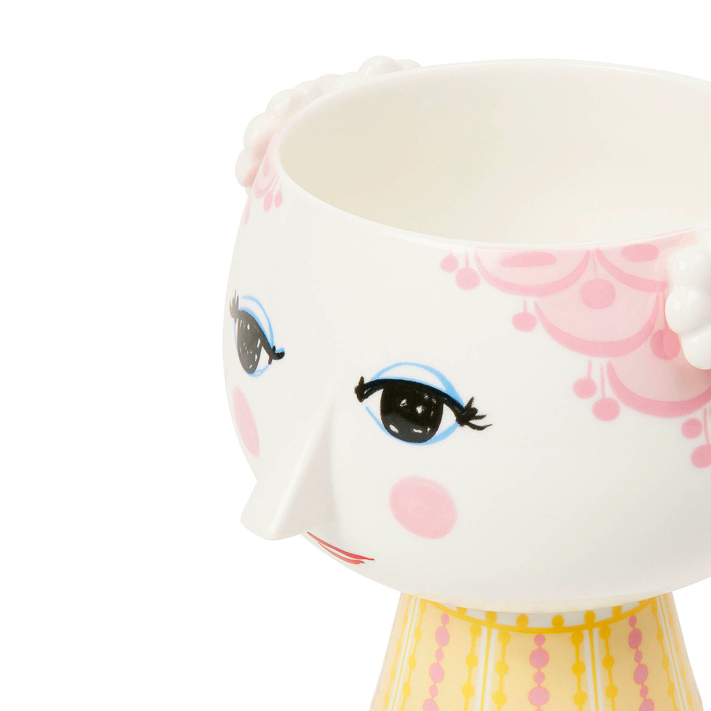 The Eva flowerpot is made of shiny glazed porcelain. The almond-shaped eyes and pointed nose are Wiinblad’s original lines, while the colourful dress pattern is a new interpretation of Bjørn Wiinblad’s illustrations from the archives. The shape is inspired by Wiinblad’s original and iconic Eva vases, which had wide heads and cone-shaped bodies. 