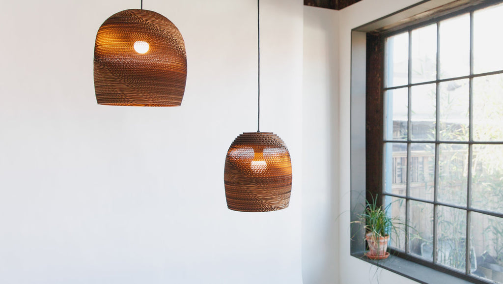 Handcrafted from 100% post-consumer recycled cardboard, our flagship Scraplights provide warm, intimate, and functional lighting for any occasion or space. Tough and elegant, each pendant is precision cut with a laser, giving the edges a slightly dark appearance and enhancing the warm light projected through the corrugation. Scraplights are assembled by hand using non-toxic adhesive and treated with a non-toxic fire retardant.