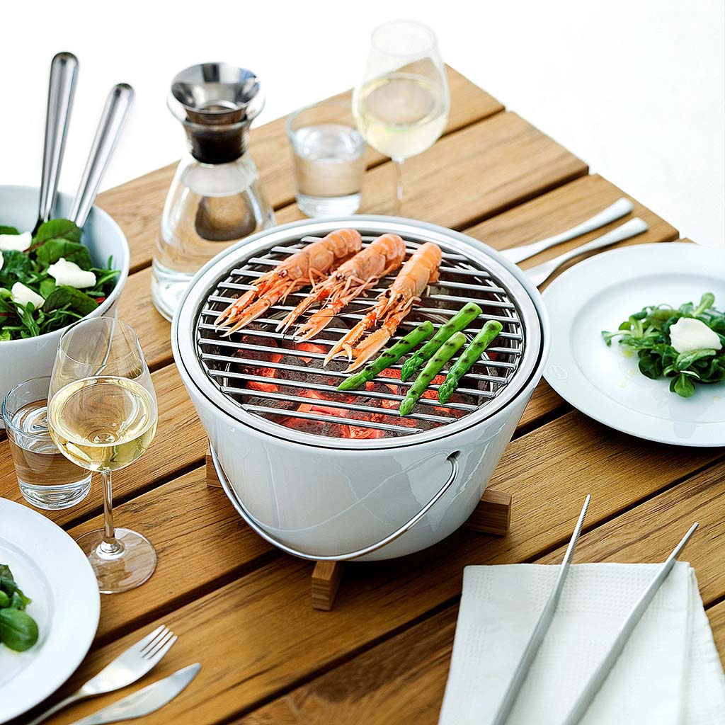 Eva Solo Porcelain Table Grill. The outside of the table grill is made of porcelain. The grid and the insert that holds the glowing coals are made of stainless steel. Prior to lighting, the grill can be lifted by the steel handle. When hot, it stands securely on its trivet.